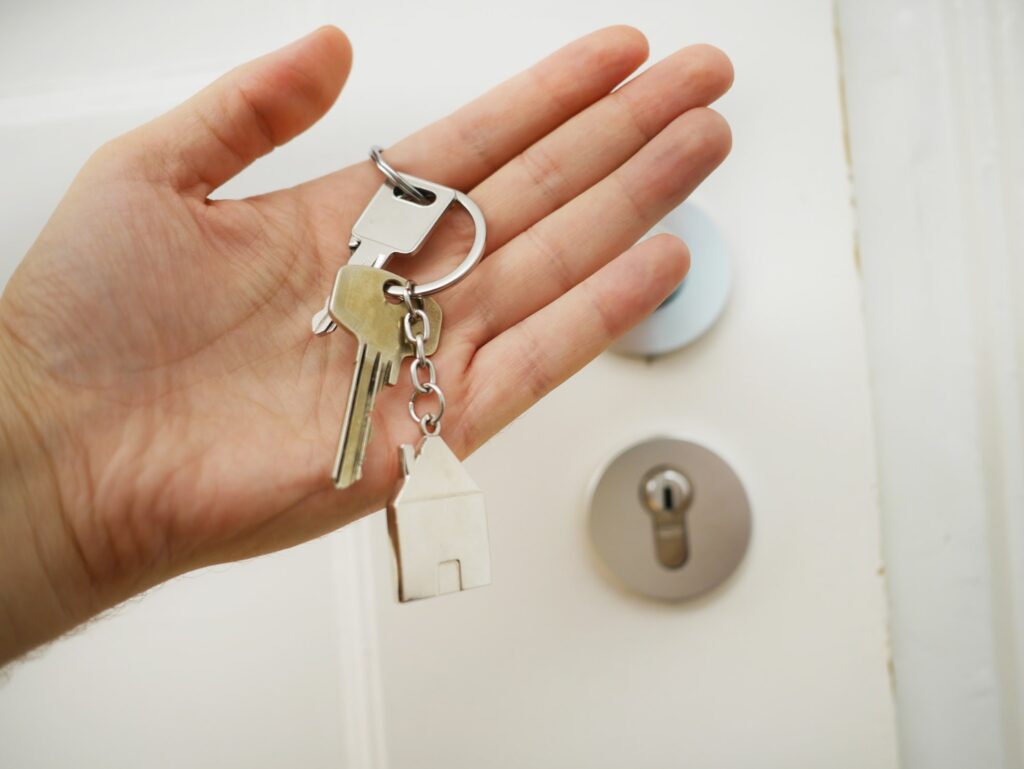 A hand holds a set of keys with a house-shaped keychain, standing in front of a door lock, dreaming of weekends at Lake Martin.