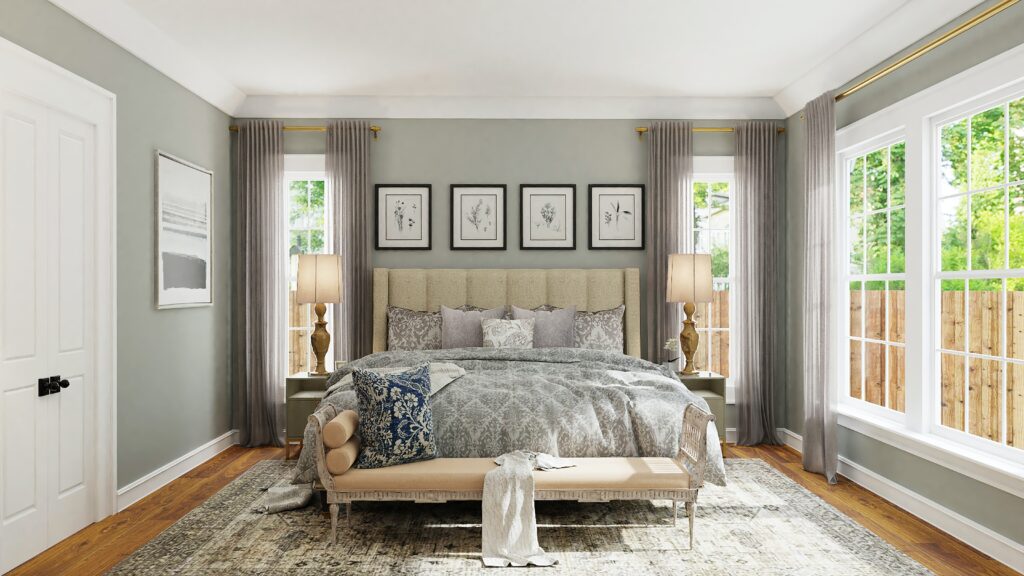 A well-lit bedroom with a large bed, light gray walls, two bedside lamps, an upholstered bench at the foot of the bed, and three framed pictures above the headboard. Large windows with views of Lake Martin flank the bed.