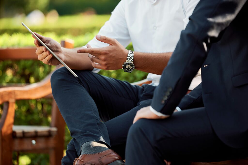 Two people sitting on a bench looking at their cell phones.