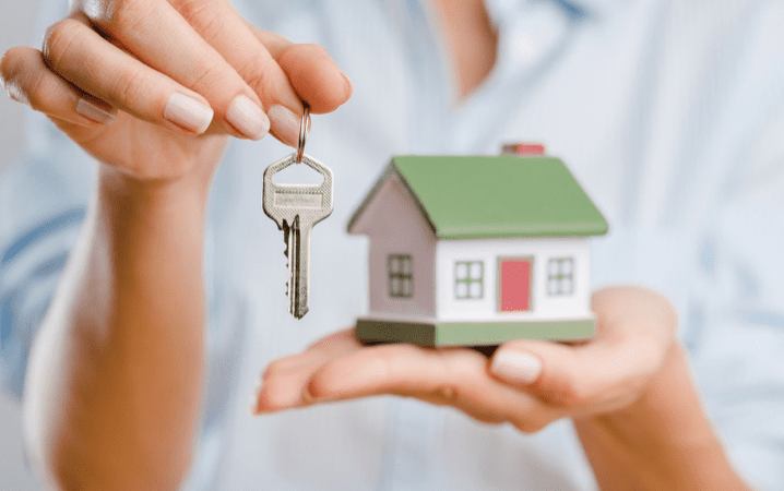 Person holding house key and model home.