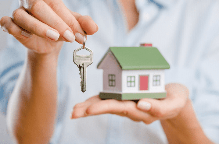 Person holding house key and model home.